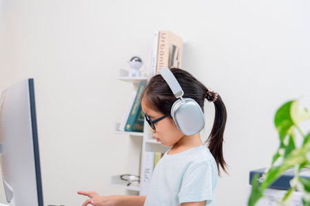 side view of asian little girl in headphones using computer at homeの写真素材