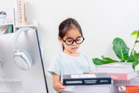 Portrait of a cute little girl in glasses reading books at homeの写真素材