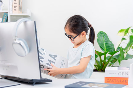 Asian little girl using computer and reading newspaper at home. Education concept.の写真素材