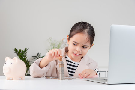 little girl wearing a cream suit analyzing coins concept of finance and investment in white roomの写真素材
