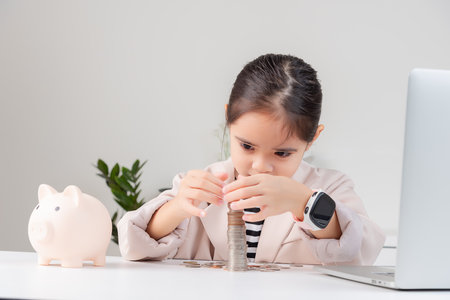 little girl wearing a cream suit analyzing coins concept of finance and investment in white roomの写真素材