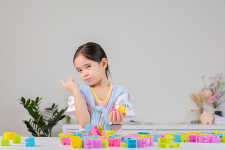 little girl wearing a bright shirt is happy Playing colorful block puzzles. in the white roomの写真素材