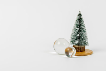 A Christmas tree is surrounded by a glass ball and a small wooden base. The scene is simple and elegant, with the tree and ball being the main focus. The white background adds a sense of calmnessの写真素材