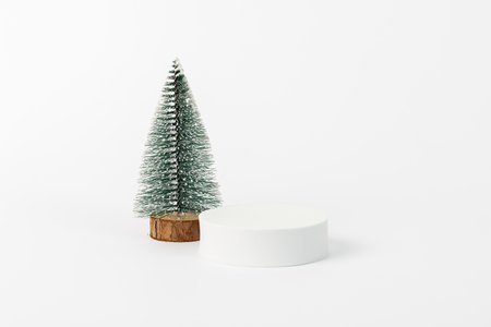 A small pine tree is standing next to a white pedestal. The white pedestal is a model of a Christmas treeの写真素材