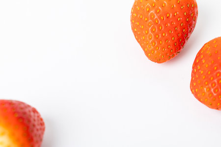 Three red strawberries on a white background. The strawberries are ripe and juicy, and their bright red color contrasts with the white background. Concept of freshness and abundanceの写真素材