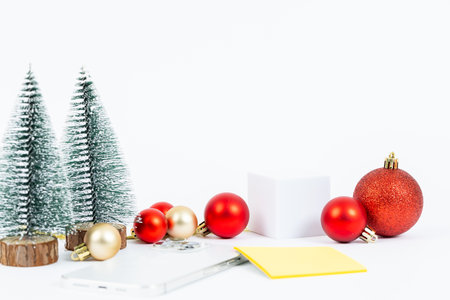 A white background with a Christmas tree and a bunch of red and gold balls. The tree is surrounded by the balls and there is a yellow notepad on the table. The image conveys a festive and joyful moodの写真素材