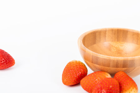 A bowl of strawberries sits on a white background. The bowl is wooden and the strawberries are redの写真素材