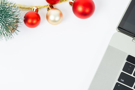 A laptop is on a table with a Christmas tree and ornaments. The laptop is open and the tree is decorated with red and gold ornaments. The scene conveys a festive and cozy atmosphereの写真素材