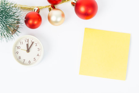 A yellow post it with a red and gold ornament on top of it. The ornament is a red ball with a gold rim. The post it is on a white backgroundの写真素材