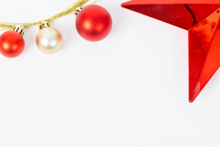 A red star sits on a white background with three red and gold balls. The star is surrounded by a white frame, and the balls are arranged in a row. Concept of festivity and celebrationの写真素材