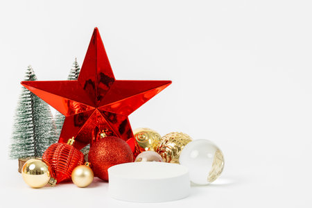A red star is surrounded by gold and white ornaments, including a white ball and a clear sphere. The scene is set in a wintery setting with a tree in the background. Scene is festive and joyfulの写真素材