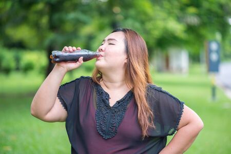Fat woman drink cola in gardenの写真素材