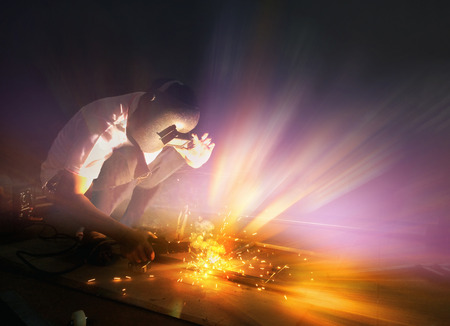 Welder making sparkle explosion while working with light gradient color. Industrial concept