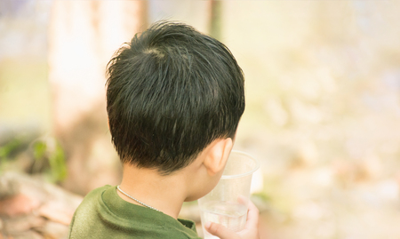 Little boy drinking water with nature background. Close up from behind and copy spaceの写真素材