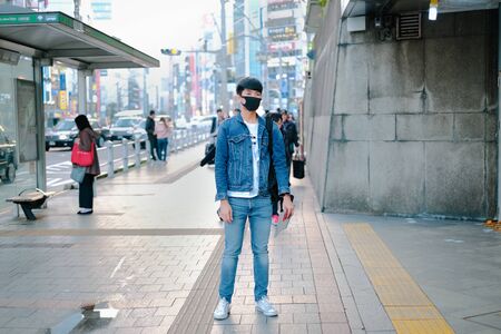 Young man standing in street wearing denim and waiting for bus to travel and japanese language on...
