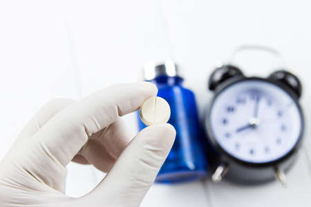Doctor hand holding medicine pill with clock and bottle, medical time conceptの写真素材