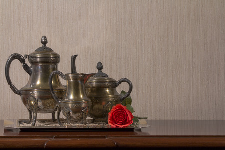 A silver tea set and red rose on a wooden desk on left sideの写真素材