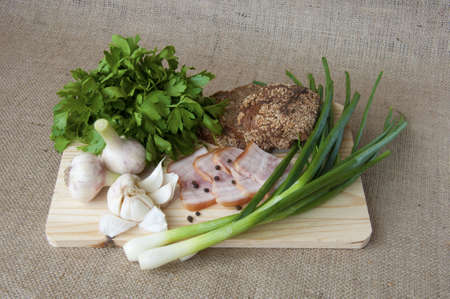on the kitchen blackboard is sliced rye bread and cereals, bacon, garlic, spices and greens against a background of rough clothの写真素材