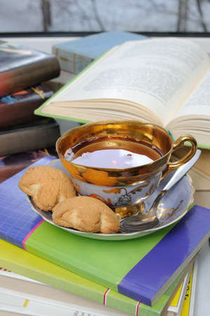 A cup of tea and biscuits on the table with booksの写真素材