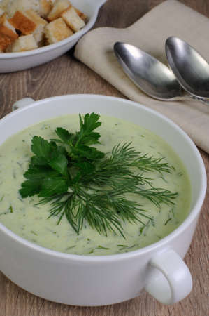 A bowl of soup with dill sauce and parsley on the table with croutonsの写真素材