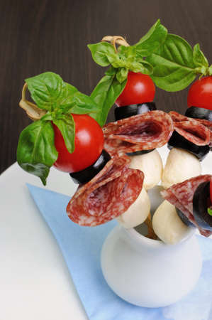 Appetizer of salami with mozzarella, olives, cherry tomatoes on skewers with basilの写真素材