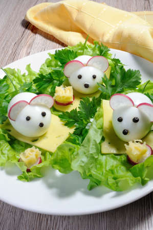 Serving a festive children's snack, boiled eggs in the form of mice in lettuce leaves and cheese cubesの写真素材