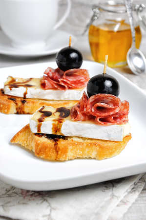 Snack from a toasted slice of baguette with soft under a noble white mold Cheese Brie, salami, a berry of grapes with honeyの写真素材