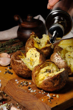 broken baked potato with spices and herbs with the addition of oil on a wooden boardの写真素材