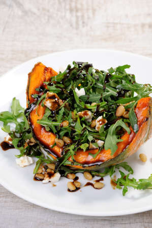 arugula serving on wedges of baked pumpkin seasoned with goat cheese with pine nuts and dressed with balsamic sauceの写真素材
