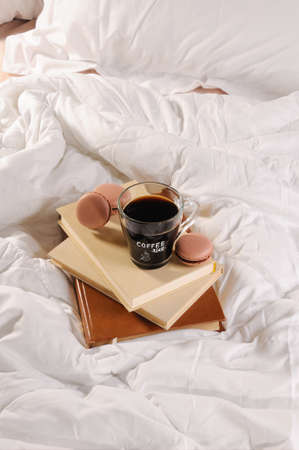 Morning cup of coffee with chocolate cakes Macaroons, on a pile of books in bed.