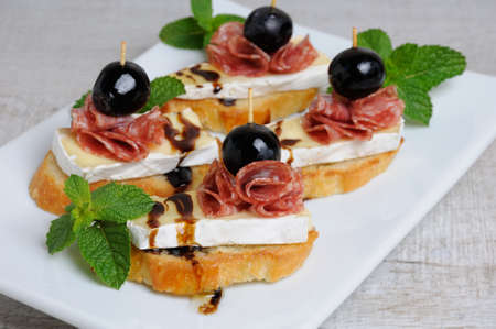 Snack from a toasted slice of baguette with soft under a noble white mold Cheese Brie, salami, a...