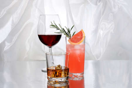 Paloma cocktail in Collins Glass, Whiskey in rocks glass with  ice cubes, red wine in...