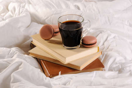 Morning cup of coffee with chocolate cakes Macaroons, on a pile of books in bed.の写真素材