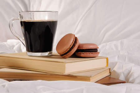 Morning cup of coffee with chocolate cakes Macaroons, on a pile of books in bed.の写真素材