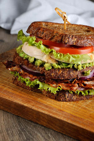 A double sandwich made of Greek bread with slices of fried bacon, avocado, boiled chicken breast, and tomatoes.の写真素材