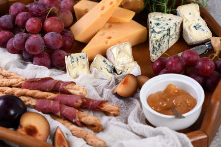 Antipasto. Dish with crispy grissini wrapped in sun-dried bacon, slices of brie cheese, camembert, blue cheese, radamer and muscat grape vine with fruit.の写真素材