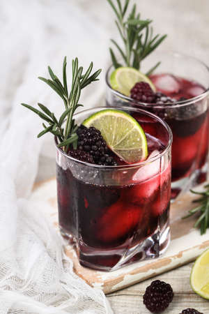 Two glasses of delicious refreshing lemonade with blackberry, ice and lime, decorated of rosemary. Cocktail on light tableの写真素材