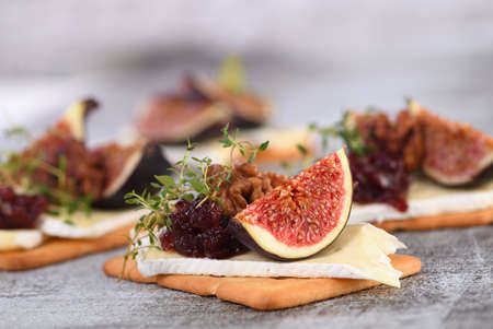 Cracker with a slice of camembert, jam, figs and nuts. A great snack idea for a holiday, picnic or party.の写真素材