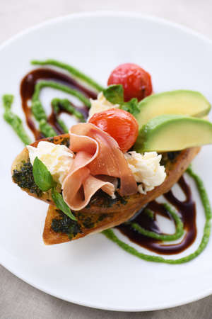 Toasted baguette toast with pesto sauce, a slice of Parma ham, mozzarella, tomato and avocado