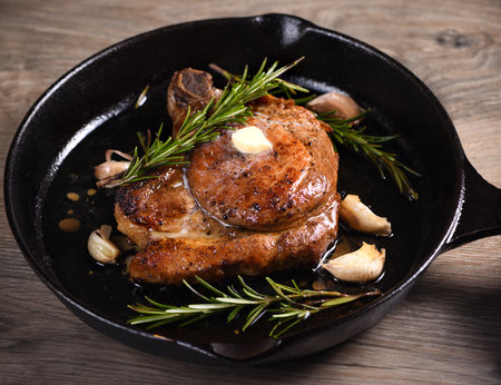Pork cutlet on the bone in a piece of butter with garlic and rosemary in a frying panの写真素材