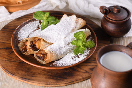 Homemade thin pancakes. The apples are cooked in a buttery caramel sauce with raisins and cinnamon and stuffed into a thin pancake. Garnish with powdered sugar and mint. Food in a rustic style.の写真素材
