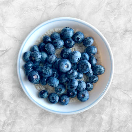 Blueberries on oatmeal in a bowl on white marbled background in top view layout, bright blue berries and oats are a healthy nutritious breakfast meal or snackの写真素材