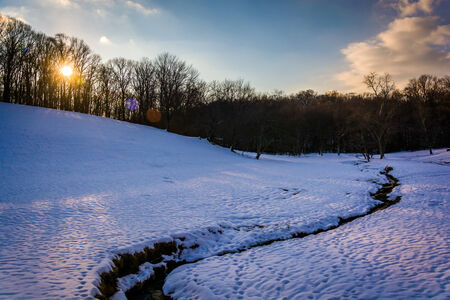 Sunset over a stream in a snow-covered field in rural Baltimore County, Maryland の写真素材