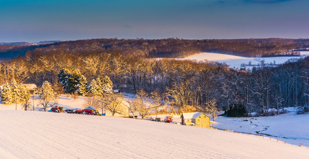 View of snow covered farm fields and rolling hills at sunset in rural York County, Pennsylvania.の写真素材