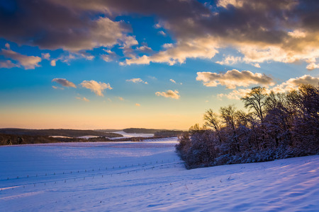 View of snow covered rolling hills and farm fields at sunset in rural York County, Pennsylvania.の写真素材