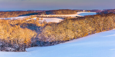 View of snow covered rolling hills and farm fields at sunset in rural York County, Pennsylvania.の写真素材