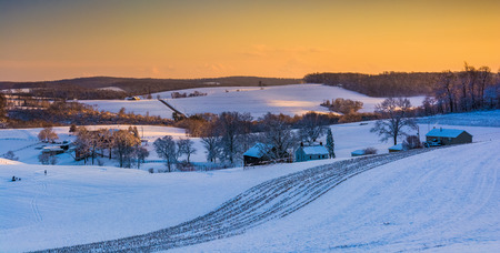 View of snow covered rolling hills and farm fields at sunset in rural York County, Pennsylvania.の写真素材