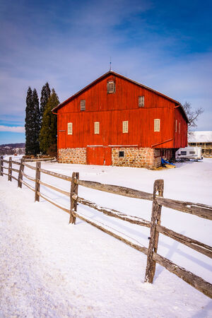 Red barn and fence in a snow-covered farm field in rural Adams County, Pennsylvania.のeditorial素材