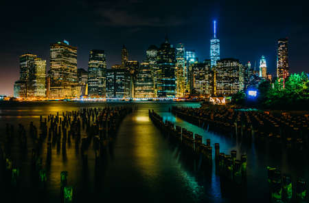 Pier pilings and the Manhattan skyline at night, seen from Brooklyn Bridge Park, New York.