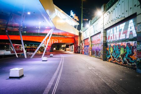 Graffiti on a wall and modern building along the Danube Canal at night, in Vienna, Austria.